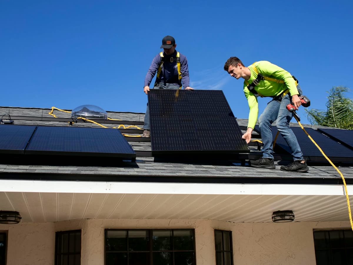 Dos técnicos instalando un panel solar en la cubierta de una vivienda